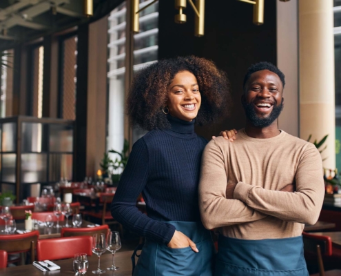 The restaurant owners smile warmly at the camera, radiating pride and joy. Their genuine expressions convey a deep satisfaction with their establishment, reflecting their dedication and love for their business. The background hints at the welcoming ambiance of their restaurant, complementing their beaming faces.