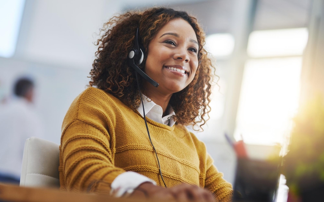 A cheerful customer service representative wears a headset and smiles while assisting a client. Her friendly and professional demeanor reflects a positive and engaging communication experience, indicating effective support and satisfaction.