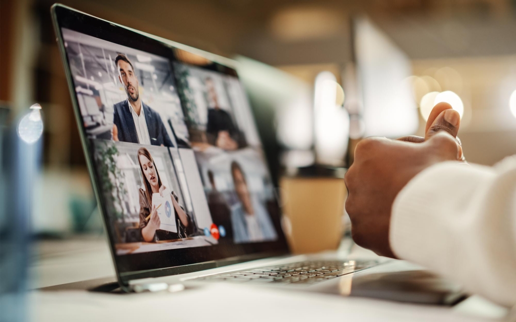 A person participates in a video conference on a laptop, where multiple colleagues are visible on the screen. The interaction is focused and professional, with the participants discussing and sharing information, demonstrating effective remote collaboration.