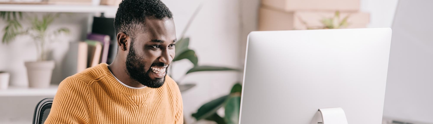 Man in a yellow shirt smiling at a computer screen