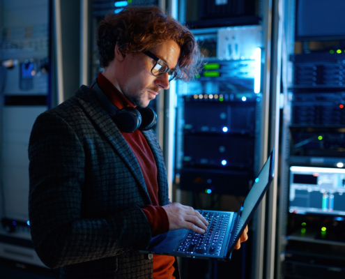 An IT professional works diligently inside a database room, surrounded by rows of servers and technical equipment. Their focused expression and attentive posture indicate precise management of data systems and a commitment to maintaining optimal performance.