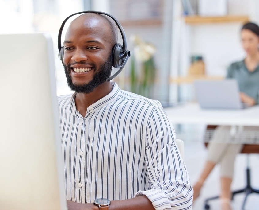 An IT employee smiles warmly while working at their desk, clearly enjoying their task. The positive demeanor and engaged posture suggest satisfaction with their work and a comfortable, productive work environment.
