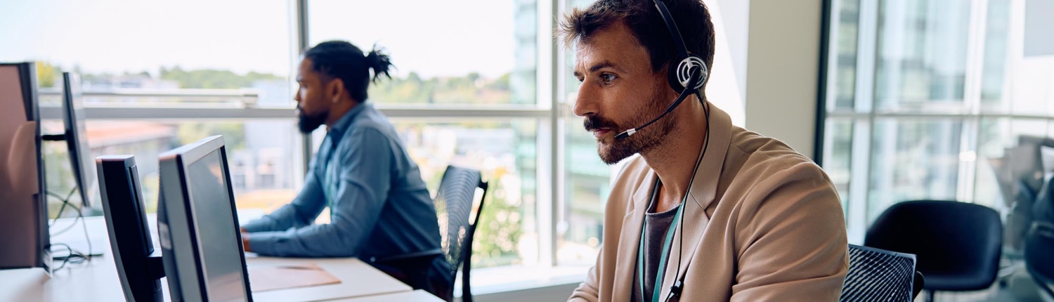 Two office colleagues efficiently handle customer service phone calls, each engaged in a conversation and providing support. Their focused expressions and coordinated effort highlight a commitment to excellent service and teamwork.