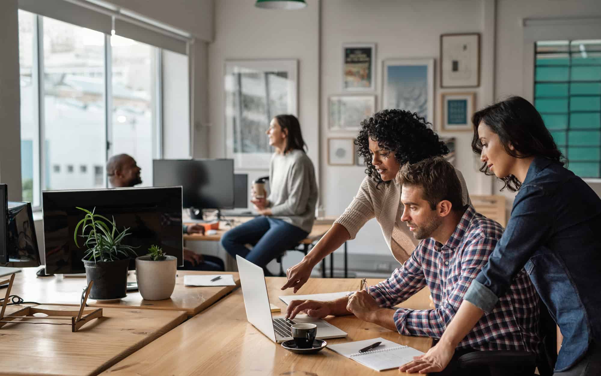 A diverse team collaborates around a conference table, engaged in a dynamic brainstorming session. Each person contributes actively, sharing ideas and reviewing documents spread across the table. Laptops, notebooks, and cups of coffee are scattered about, reflecting a productive and focused environment.