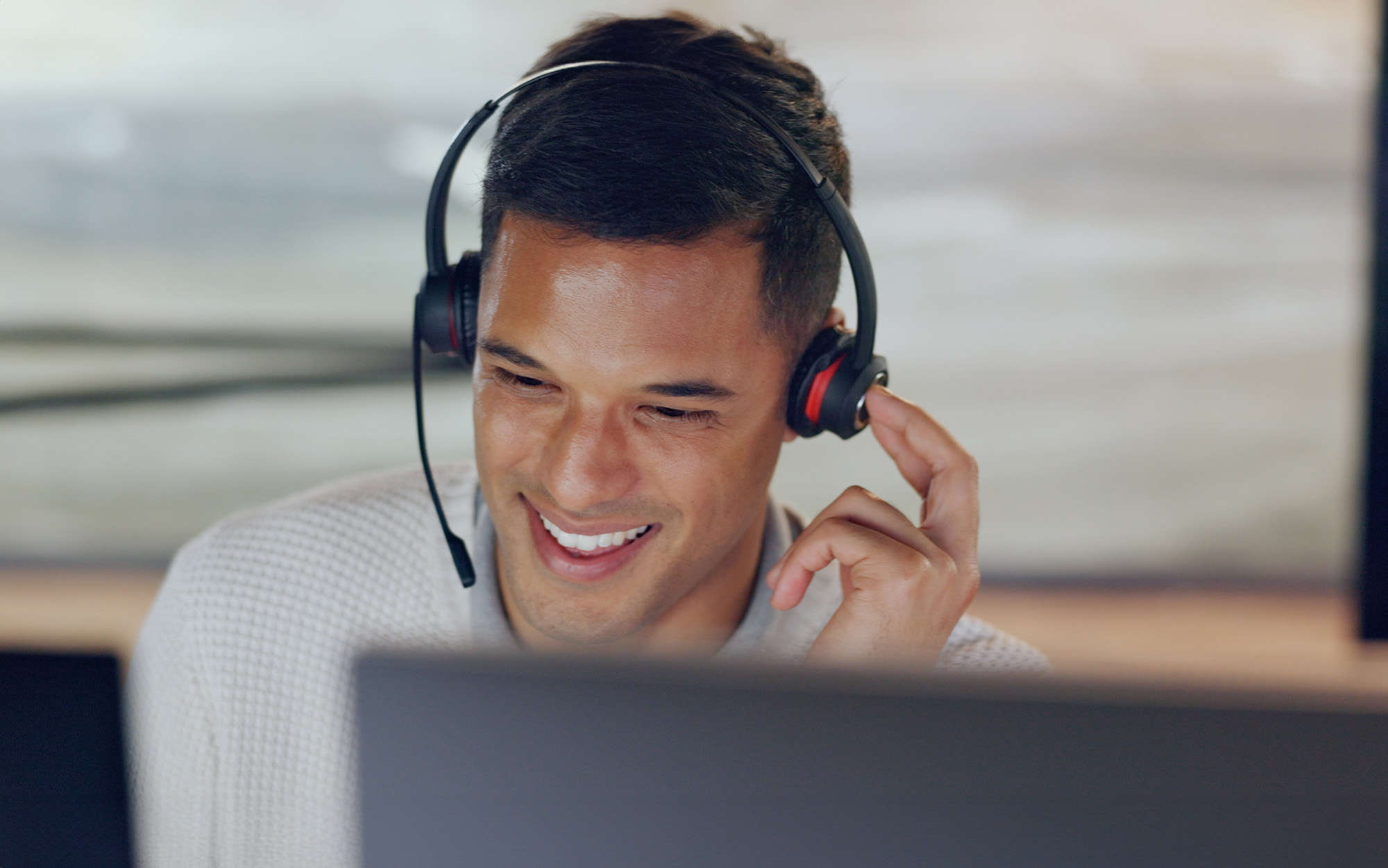 A smiling customer support representative wearing a headset, engaging in a call and providing assistance while using a computer.