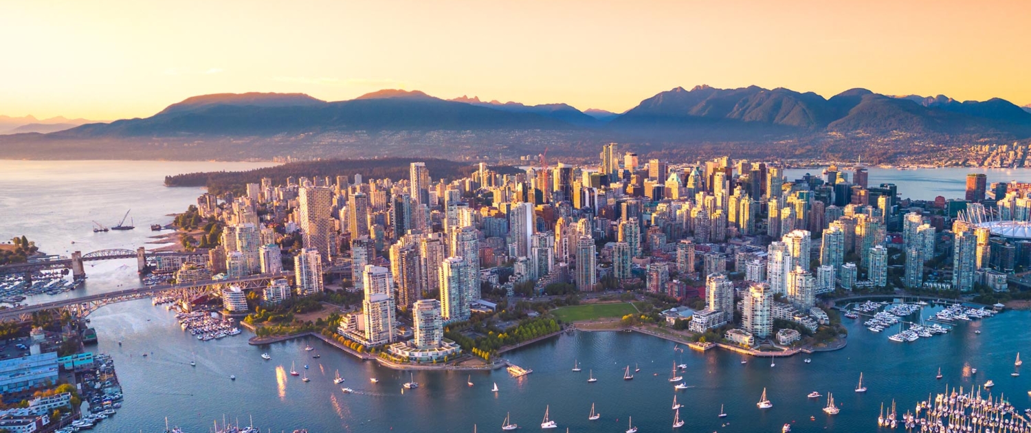 An aerial view of Vancouver's skyline at sunset, showcasing a bustling harbor filled with sailboats, modern high-rise buildings, and the surrounding mountains, all bathed in a warm, orange glow.