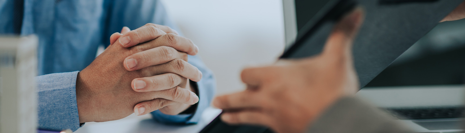 A close-up shot of a business meeting, focusing on the hands of two individuals discussing documents with a clipboard and laptop on the table, representing collaboration and decision-making.
