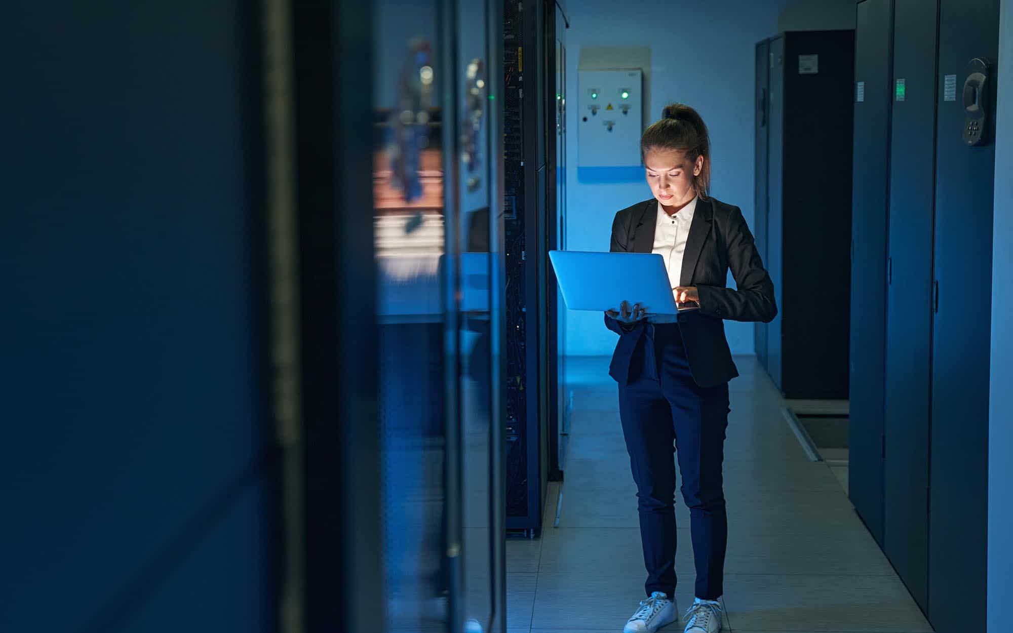 Female technician using laptop to analyze server in data center